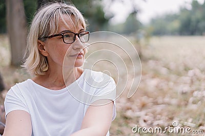 Elderly women caucasian wear glasses while sitting think at the public park in the autumn Stock Photo