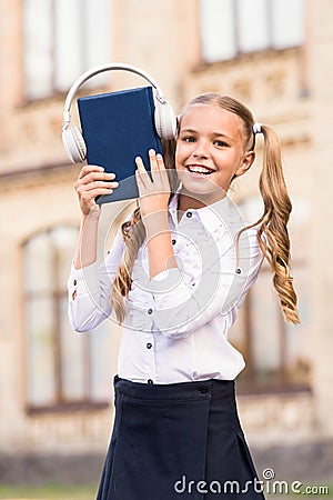 Elearning and modern methods. Girl cute schoolgirl hold book and headphones. Knowledge assimilate better this way. Audio Stock Photo