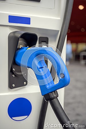 Gun with a powerful cable for charging an electric vehicle is inserted into the socket of the charging station column while Stock Photo