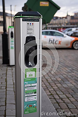 Electric car charging point with Tesla car plugged in decorated with Bitcoin and Nasdaq logotypes. Editorial Stock Photo