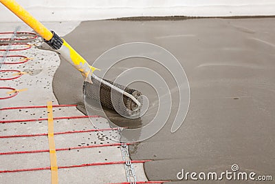 Electric floor heating system installation in new house. Worker align cement with roller. Stock Photo