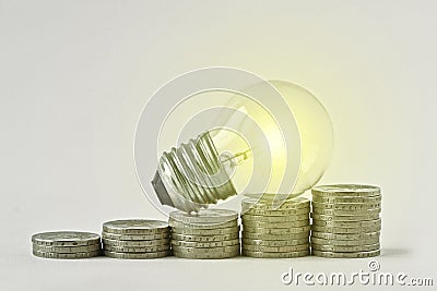 Electric light bulb on raising piles of coins - Concept of increase in electricity bills Stock Photo