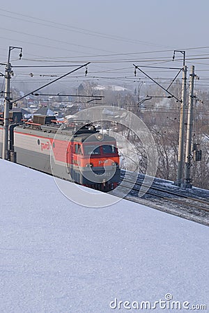 An electric locomotive rides along a snow embankment. Editorial image. Editorial Stock Photo
