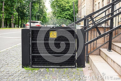 Electric platform lift at building staircase for disabled people with wheelchair sign plate on old city street. Elevator Stock Photo