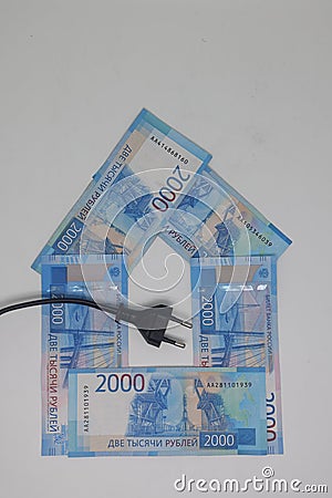 The electric plug lies on the banknotes laid out in the form of a house, electricity savings, energy crisis. expensive Stock Photo