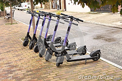 Electric scooter for rent, sharing. Six purple Electric Scooters are parked on sidewalk. Front view Editorial Stock Photo