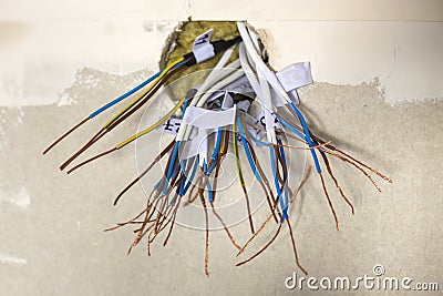 Electrical exposed connected wires protruding from socket on white wall. Electrical wiring installation. Finishing works in Stock Photo