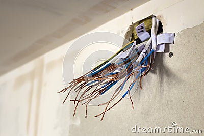 Electrical exposed connected wires protruding from socket on white wall. Electrical wiring installation. Finishing works in Stock Photo