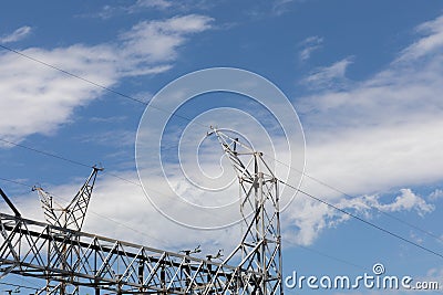 Electrical power lines entering a power transfer station, gridded trusses against a blue sky with clouds Stock Photo