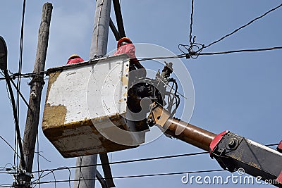 Electrical Workers On Telehandler With Bucket installing High tension wires on tall concrete post. Underside view low angle Editorial Stock Photo