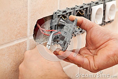 Electrician hands installing wires into a wall fixture Stock Photo