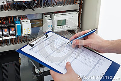 Electrician holding clipboard while examining fusebox Stock Photo