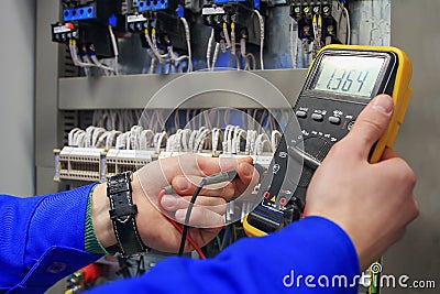 Electrician measures voltage with multimeter in electrical cabinet. Stock Photo