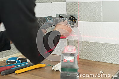 Electrician using infrared laser level to install electrical outlets. Renovation and construction in kitchen Stock Photo