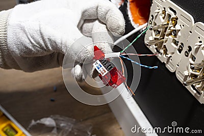 An electrician in white gloves is installing a network cable for the RJ45 module to the computer socket in the room. Stock Photo