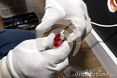 An electrician in white gloves is installing a network cable for the RJ45 module to the computer socket in the room. Stock Photo