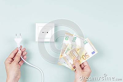 Electricity cost and expensive energy concept. Female hands holding electric power plug and Euro money banknotes near Stock Photo