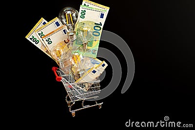 Electricity cost. Light bulbs set and euro banknotes in a supermarket trolley on a black background.Payment of Stock Photo