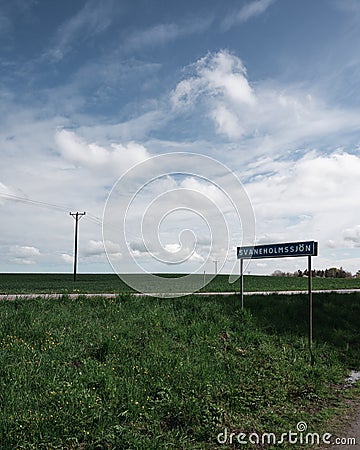 Electricity poles on green famlands next to a rural road and a street sign with the name of the nearby lake SvaneholmssjÃ¶n on a Stock Photo