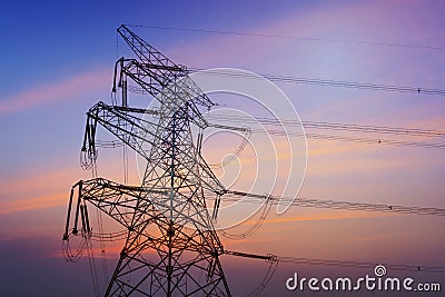 Electricity pylons, power lines and trees silhouetted against a cloudy sky Stock Photo