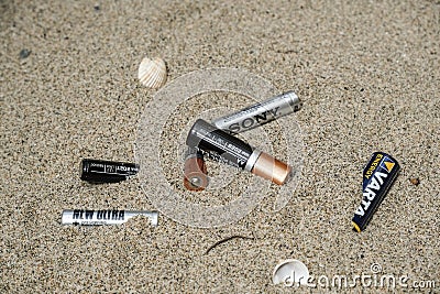 Electronic discarded battery waste on sandy sea coast ecosystem, sea pollution disease Editorial Stock Photo