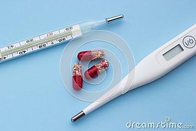 Electronic and mercury thermometer with red-yellow pills on a blue background Stock Photo