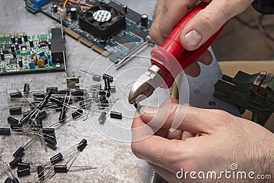 An electronic service worker cuts the tip of the capacitor with a pliers. Stock Photo