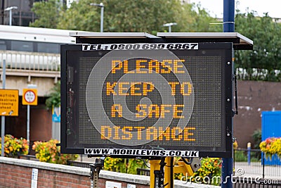 An electronic signboard outside a train station stating please keep a safe distance during the coronavirus pandemic Editorial Stock Photo