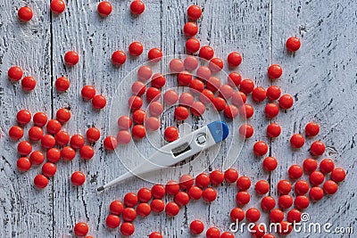 An electronic thermometer with a high temperature mark of 39.7 among many bright red pills on a wooden white table. Stock Photo