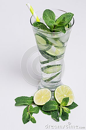 Elegance high glass with cold natural refreshing cocktail with slices cucumber, lime, mint, ice, straw on white wood plank. Stock Photo