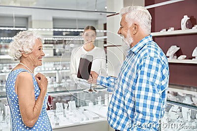 Elegant aged woman trying on pearl necklace at jewelry store Stock Photo