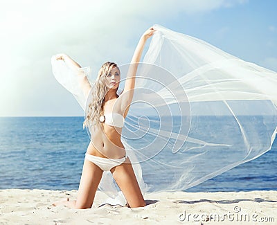Beautiful, attractive blond posing with a blowing fabric on the beach. Holiday, vacation, concept. Stock Photo