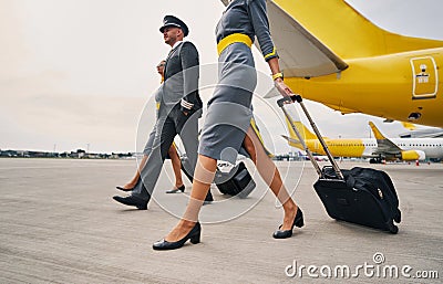 Elegant aviator and two stylish stewardesses with luggage moving ahead Stock Photo