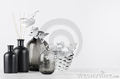 Elegant blank black bottles, glass vase for home decor on soft light white wood table with silver leaves as template. Stock Photo