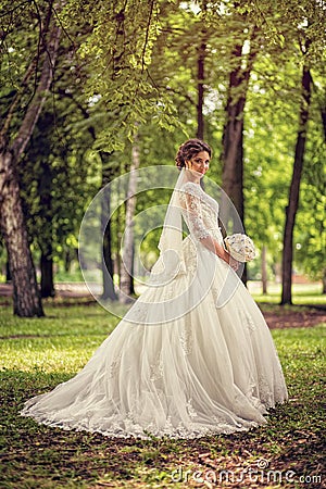 Elegant bride in wedding dress with dipped hem in full length on a background of a forest or Park Stock Photo