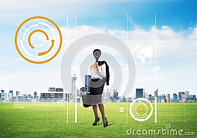 Camera headed woman standing on green grass against modern cityscape Stock Photo