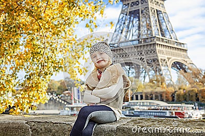 Elegant child sitting on parapet on embankment near Eiffel tower Stock Photo