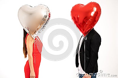 Elegant couple stands against each other, covering their faces with silver and red air balloons, St. Valentine`s day Stock Photo