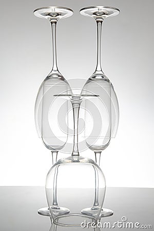 Elegant empty wine glasses with delicate stems arranged neatly, reflecting on a shiny table, set against a minimalist gray Stock Photo