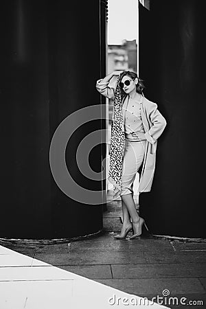 Stylish blonde girl in pink clothes and sunglasses posing in the city on a background of black huge barrels Stock Photo