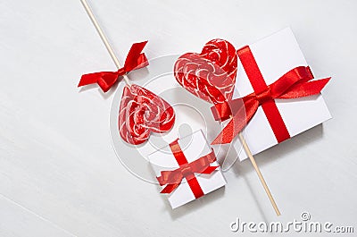 Elegant gentle wedding background - white gift boxes with red bow, sweet lollipops hearts on white wood board, top view. Stock Photo