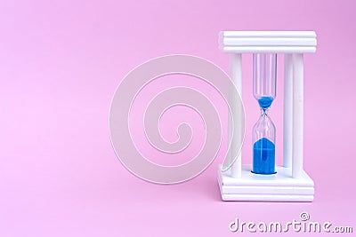 Elegant hourglass with running blue sand on pink backgroun Stock Photo