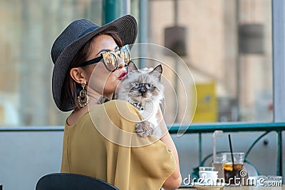 Elegant Italian woman with hat and glasses kisses her cat Stock Photo
