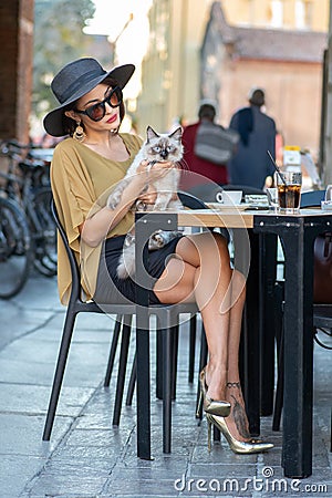 Elegant Italian woman with hat and glasses pets her cats Stock Photo