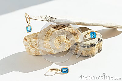 Elegant jewellery set of golden ring andearrings with blue topaz on white background with stones and wood. Minimal style Stock Photo
