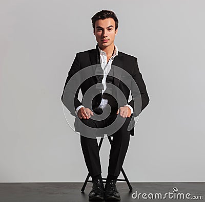 Elegant man in suit and undone bowtie sitting on chair Stock Photo