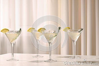 Elegant martini glasses with fresh cocktail, rosemary and lemon slices on white table indoors Stock Photo