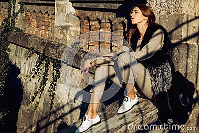 Elegant model in rich outfit and fluffy fur coat. Beautiful young girl with a chic figure and long dark hair walks at Stock Photo