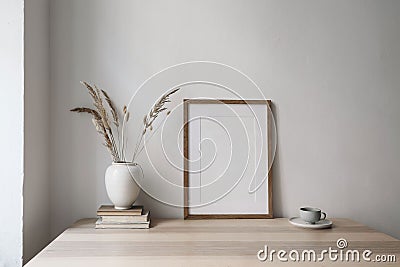 Elegant neutral poster mockup. Wooden picture frame mockup on beige table. Vase with dry grass and old books, cup of Stock Photo