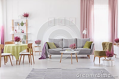 Elegant daily room with round table with wooden chairs and grey sofa with olive green pillows, stylish armchair next to it Stock Photo